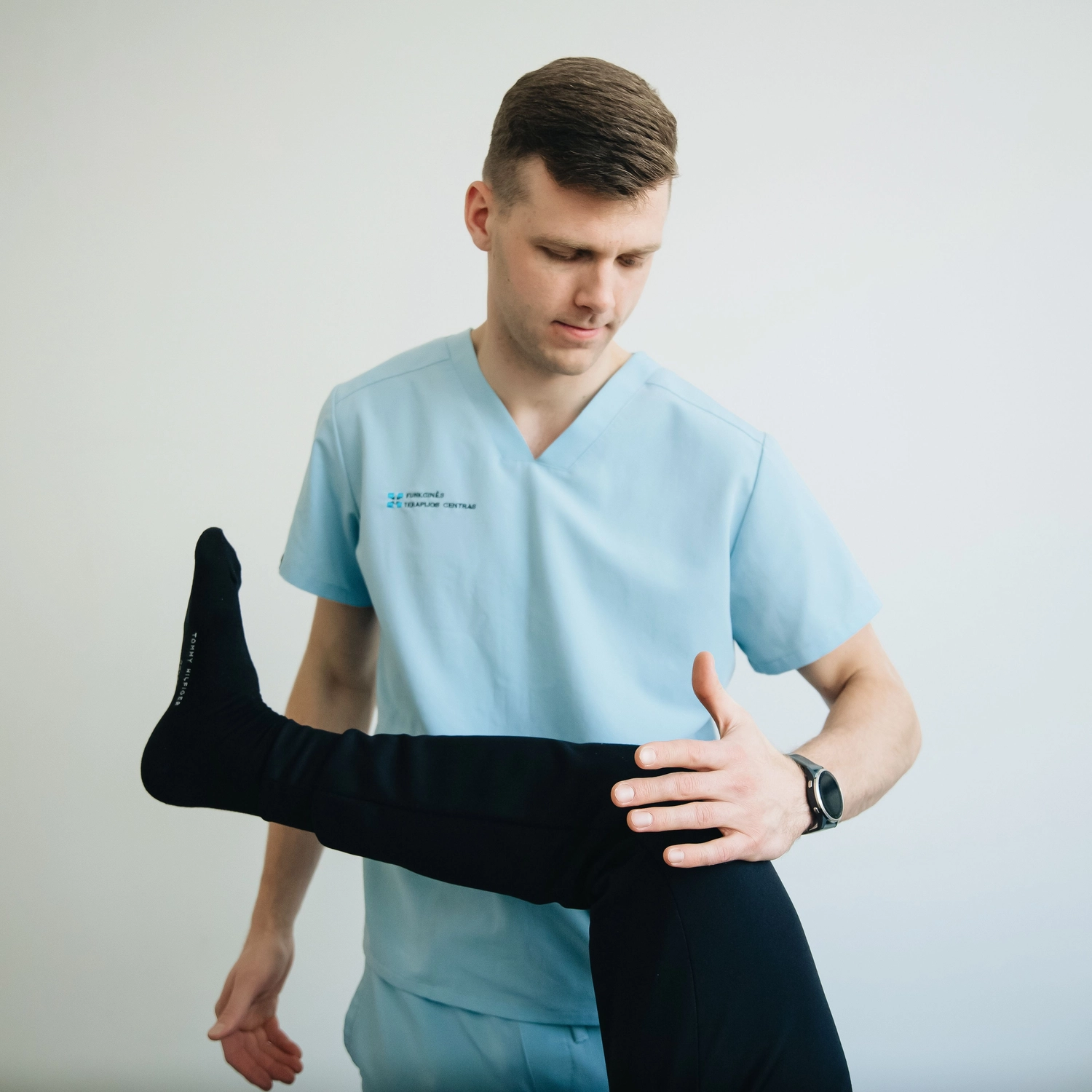 Physiotherapie Balance - Physiotherapie - Eine medizinische Fachkraft in hellblauer OP-Kleidung untersucht das Bein eines Patienten, das an Hüfte und Knie gebeugt ist.